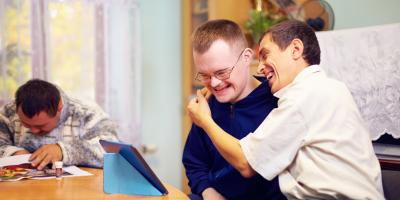 Image of 3 people at a table, 2 hugging while looking at a tablet