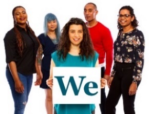 A group of people. There is a woman at the front of the group, she is holding a card that has We written on it. 