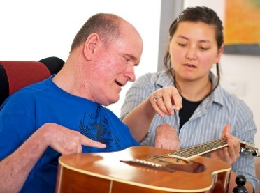 A woman showing a man with disability how to play a guitar.